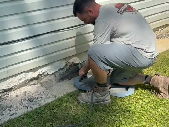 Gibson crew chipping deteriorated mortar from a residential foundation